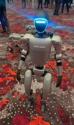 Un robot Unitree G1 gris, visage lumineux bleu, debout sur une moquette rouge dans un salon professionnel.